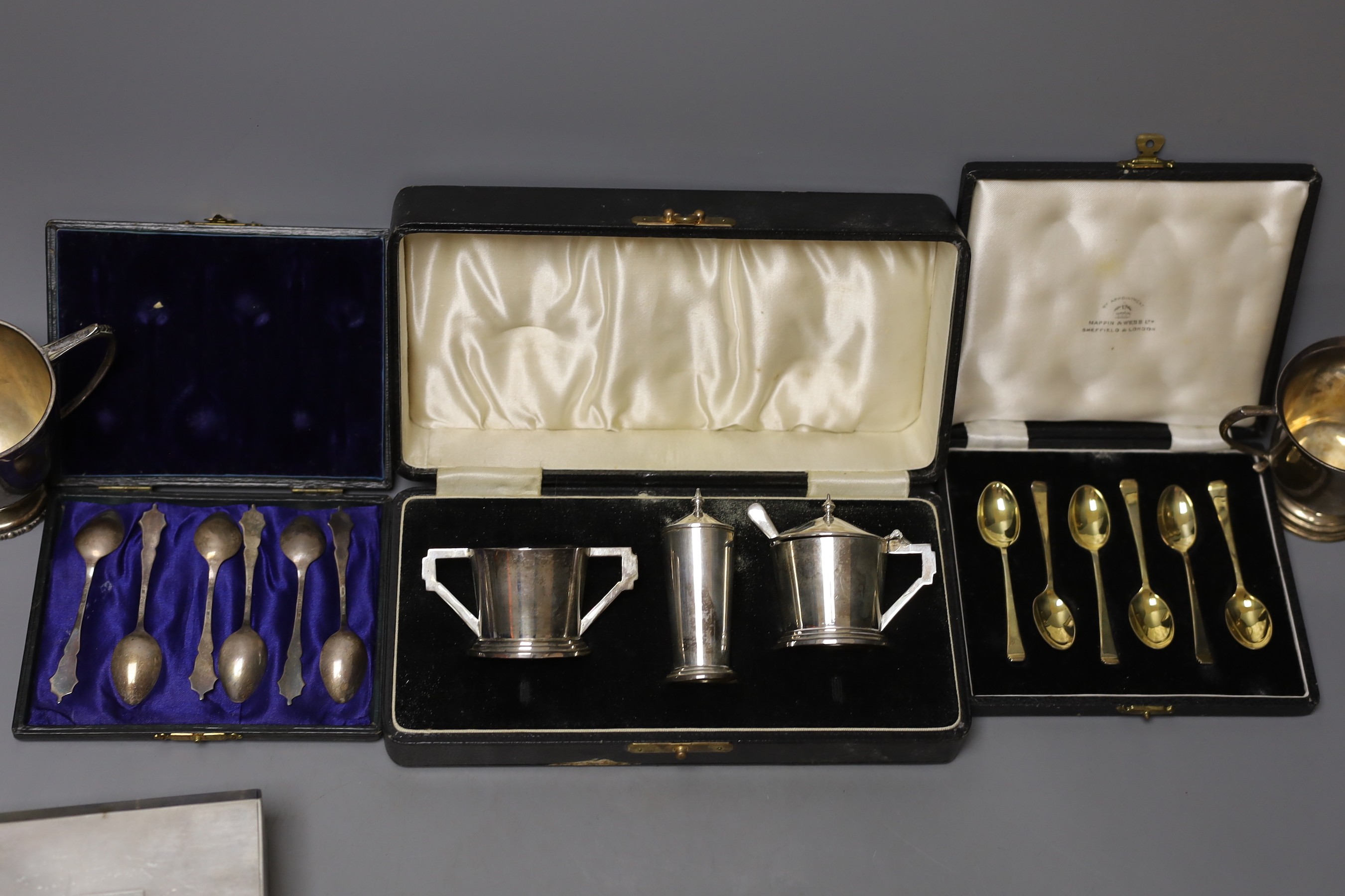 A group of mixed silver, including a cigarette box, two silver christening mugs, two similar pierced bonbon dishes, a cased Art Deco three piece condiment set, two cased sets of six teaspoons one enamelled stamped sterli